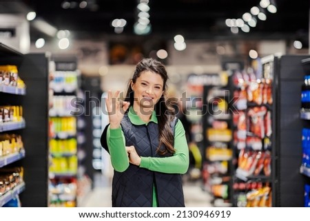 A supermarket female manager gesturing okay sign for good prices and discount.