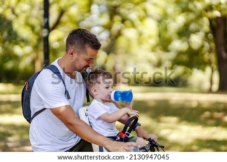 Little boy drinking refreshment from bottle while taking a break from cycling with his father.