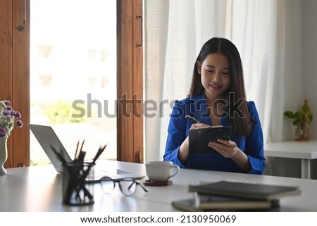 A portrait of a young pretty businesswoman wearing a suit sitting in the office working on a document and a laptop, a cup of coffee and glasses, for business, finance and insurance concept