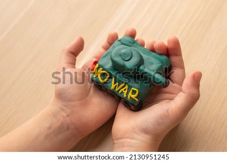 Children's hands hold a plasticine tank with the inscription No war. A call to stop the war. There is no war. Stop war.