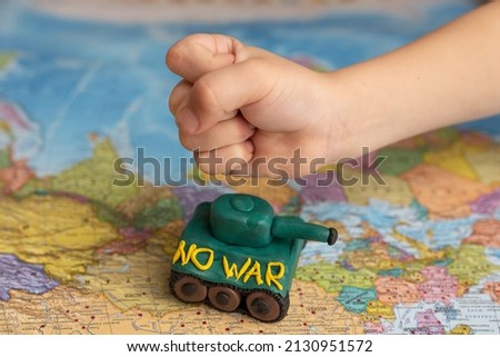 A little boy punches a tank on the background of a map of the worlds. A symbol of peace. Stop war. No war