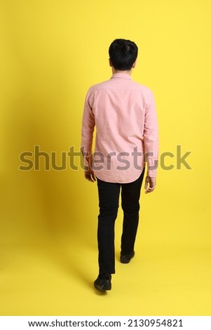 The Asian man with pink shirt standing on the yellow background.