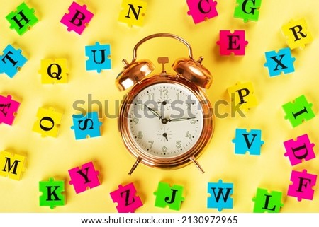 Top view of gold alarm and english alphabet from multi-colored puzzles around it. Simulator for learning English. Educational process. School, lessons, pedagogy. The concept of thinking development