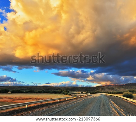 Improbably beautiful huge storm  cloud is shined with the sunset. The cloud hangs over the gravel road
