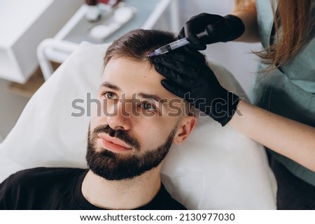 An attractive man receives mesotherapy injections to treat hair loss at the clinic. Injections into the skin and scalp Royalty-Free Stock Photo #2130977030