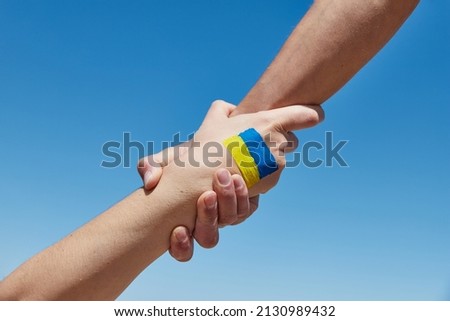 Lend a hand help painted in ukrainian flag colors against blue sky. Stand with Ukraine Royalty-Free Stock Photo #2130989432