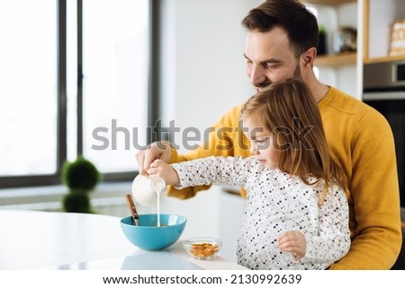 Father and his small girl  having cereal for breakfast  in the kitchen  while they pouring  milk into the bowl Royalty-Free Stock Photo #2130992639