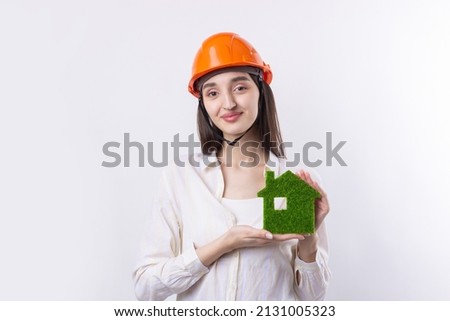 A young girl architect in a construction helmet demonstrates a model of a green house. Sale of ecological real estate.