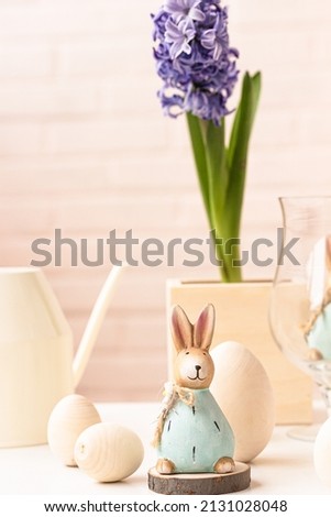 Easter rabbit, blue blooming hyacinth flower, eggs, watering can on beige background. Easter decoration conceptn
