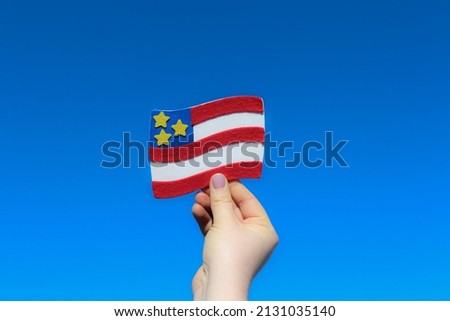 A hand holding USA symbolic flag. USA Strong Nation. Patriotism. Clear blue sky background. 
