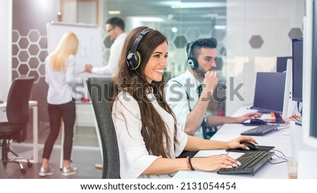 Young positive woman customer support phone operator in microphone headset working on computer in the office Royalty-Free Stock Photo #2131054454