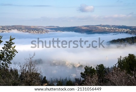 A low cloud in a valley among the Judea mountains, covering some of the Jerusalem, Israel, suburbs, at dawn. Royalty-Free Stock Photo #2131056449