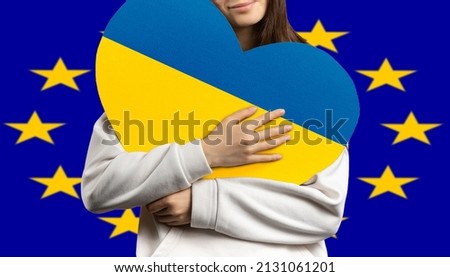 A girl holds a heart to her chest with the flag of Ukraine, and behind her the flag of the European Union 
