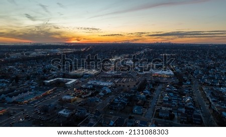 Aerial, high angle drone view high over a busy Long Island town during a colorful sunset. Street lights are turned on. The roads have some traffic and movement.