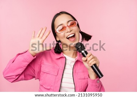 Happy beautiful asian girl singing with mic, using microphone, enjoying karaoke, posing against pink studio background Royalty-Free Stock Photo #2131095950