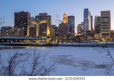 The Hennepin Ave Suspension Bridge and Minneapolis Skyline Illuminated during a Winter Blue Hour over the Frozen Mississippi River