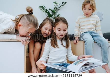 Entertained children gathered in a room to read a picture book, all looking at it. From five to eight years of age.