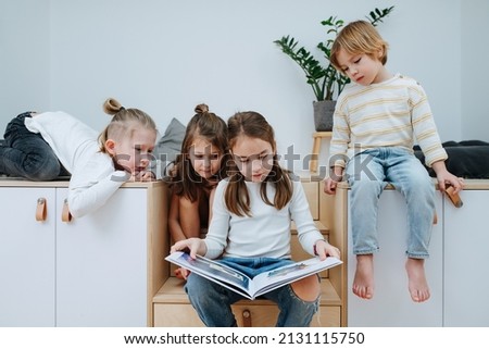 Bored children gathered in a room to read a picture book, all looking at it. From five to eight years of age.