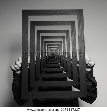 Enigmatic surrealistic optical illusion. A man holding picture frame. Royalty-Free Stock Photo #2131117337