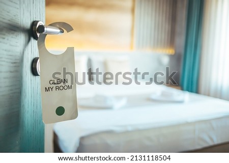 Opened door of hotel room. Door of hotel room with please make up room sign. Hotel room or apartment doorway with key and keyring key fob in open door and bedroom in background