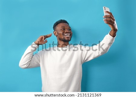 Portrait of a happy African-American man taking a selfie and smiling on a blue isolated background