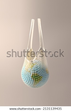World globe in crochet bag, floating in air on beige background. Eco-friendly life in the style of zero waste. Earth day, save the planet. Royalty-Free Stock Photo #2131139435