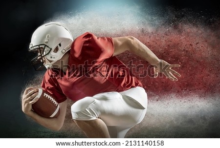 American football sportsman player with ball in action on stadium under lights of background. Sport, proud footballer in white helmet and red t-shirt ready to play.