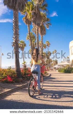 Attractive young woman riding bike near beach with palm trees, Santa Monica, Los Angeles, California