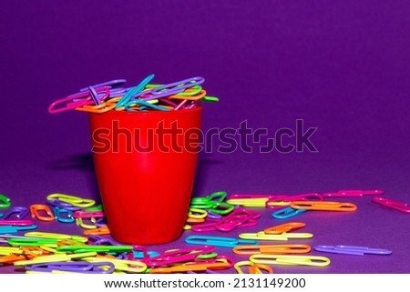 red cup full of colorful staples that fall out and around on a purple background