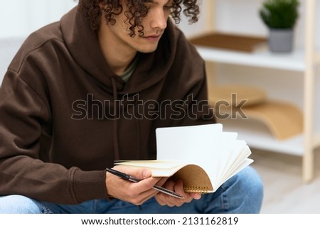 A young man writes in a notebook sitting on a chair in the room Lifestyle