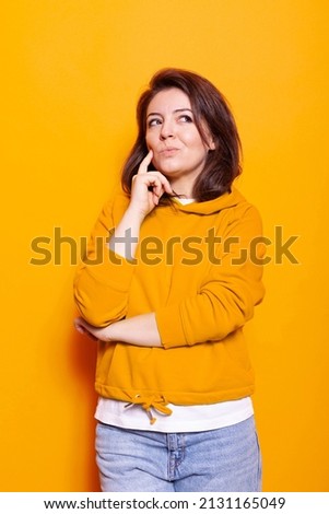Caucasian woman thinking with hand on chin at camera in studio. Thoughtful person feeling confused and wondering about idea and question. Pensive adult showing contemplative expression Royalty-Free Stock Photo #2131165049