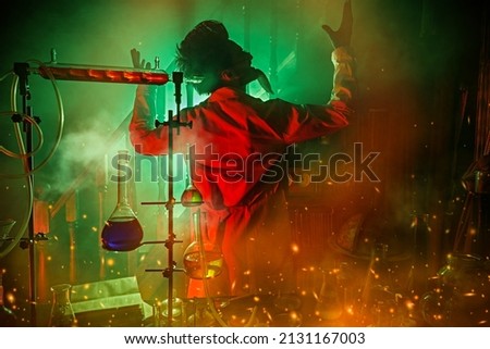 A mad scientist, obsessed with his idea, conducts scientific experiments in his laboratory, illuminated by a mysterious red and green light. Science fiction. Vintage style. Royalty-Free Stock Photo #2131167003