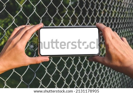 Close-up. Smartphone mockup in woman's hands. Against the background of a steel wire fence and nature