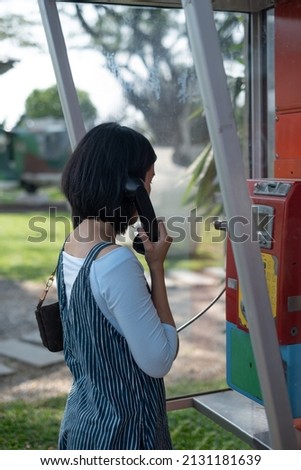 Woman using old style public pay phone in telephone booth. Royalty-Free Stock Photo #2131181639