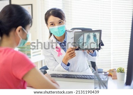 asian woman has breast cancer diagnosis in hospital - female doctor showing mammography test results and xray to patient on digital tablet while they wear protective face mask to prevent COVID19
