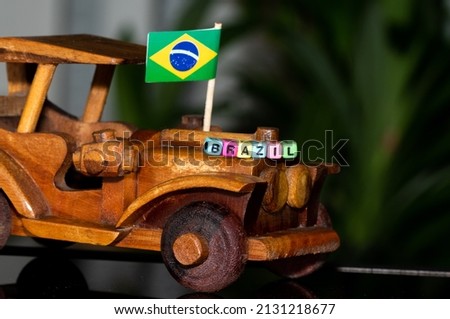 Mote alphabet blocks arranged into "Brazil" on a miniature wooden car on the background of the national flag.