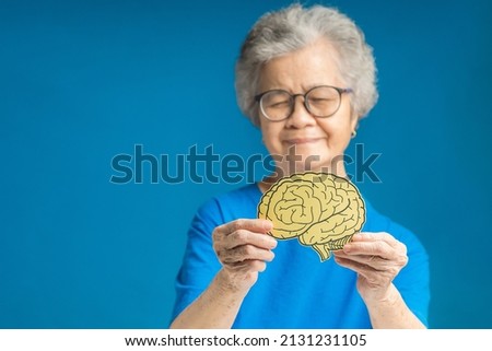 Hands of a senior woman holding a brain shape made from yellow paper against a blue background. Alzheimer's, Parkinson's disease, dementia, stroke, seizure, or mental health. Healthcare concept Royalty-Free Stock Photo #2131231105