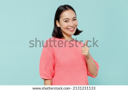 Young smiling fun happy woman of Asian ethnicity 20s wearing pink sweater showing thumb up like gesture isolated on pastel plain light blue color background studio portrait. People lifestyle concept Royalty-Free Stock Photo #2131231133