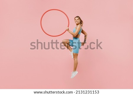 Full length young strong sporty athletic fitness trainer instructor woman wear blue tracksuit spend time in home gym hold hula hoop isolated on pastel plain light pink background Workout sport concept