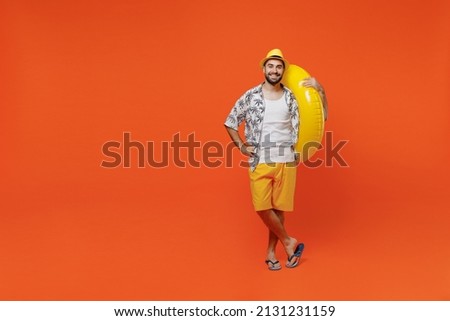 Full body young smiling cheerful fun cool tourist man wear beach shirt hat hold inflatable ring look camera isolated on plain orange background studio portrait Summer vacation sea rest sun tan concept Royalty-Free Stock Photo #2131231159