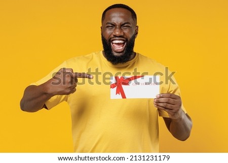 Young smiling happy black man 20s wearing bright casual t-shirt point finger on gift certificate coupon voucher card for store isolated on plain yellow color background studio People lifestyle concept