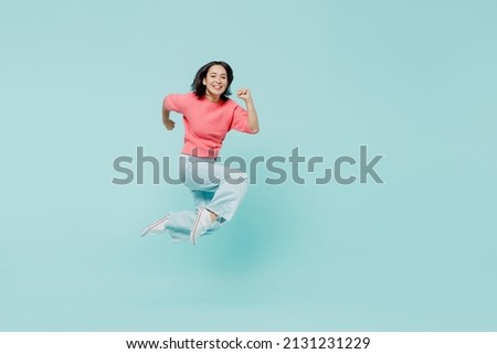 Full body young smiling happy woman of Asian ethnicity 20s wear pink sweater jump high run fast hurry up isolated on pastel plain light blue color background studio portrait. People lifestyle concept Royalty-Free Stock Photo #2131231229
