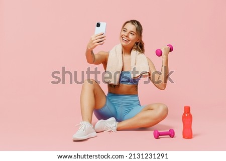 Full size young fitness trainer instructor woman wear blue tracksuit spend time in home gym do selfie on mobile cell phone hold dumbbells isolated on plain light pink background. Workout sport concept