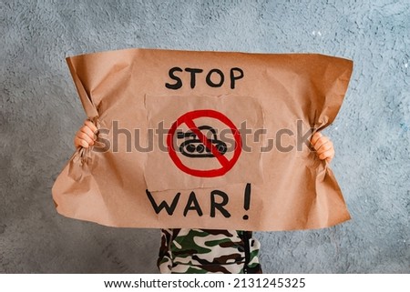 child raises a banner with the inscription no war, standing on the gray concrete background of the studio. No war, stop the war, peace