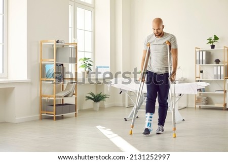 Orthopaedic recovery. Man wearing support adjustable fracture fixator on injured leg walks on crutches in hospital office. Concept of rehabilitation of people after serious physical accident injury. Royalty-Free Stock Photo #2131252997