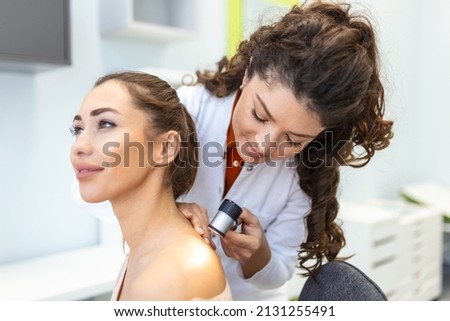 Female dermatologist carefully examining the skin of a female patient using a dermascope, looking for signs of skin cancer. Dermatologist examining patient's birthmark with magnifying glass in clinic Royalty-Free Stock Photo #2131255491
