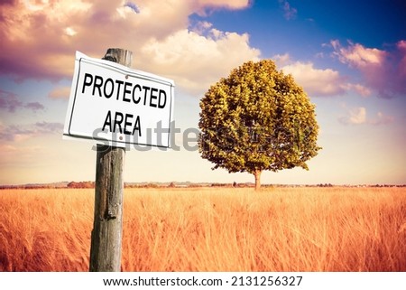 Protected area written on a field sign with an lone tree in a golden wheat field - Sign indicating in the countryside - concept image.