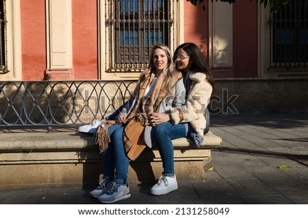 lesbian couple sitting on a bench in a monumental square in the city. They are very happy and resting when they arrive in the city on holiday. Concept tourism and travel. lgtb