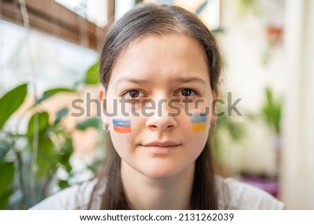 Portrait of young Russian-Ukrainian girl with the flag of Ukraine and Russia on her face. The concept of participation of the Ukrainian people in the war with Russia. Not war concept. quality photo