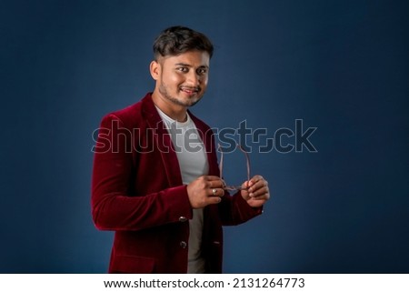 Portrait of Happy Indian young man wearing a blazer with eyeglasses posing on a blue background